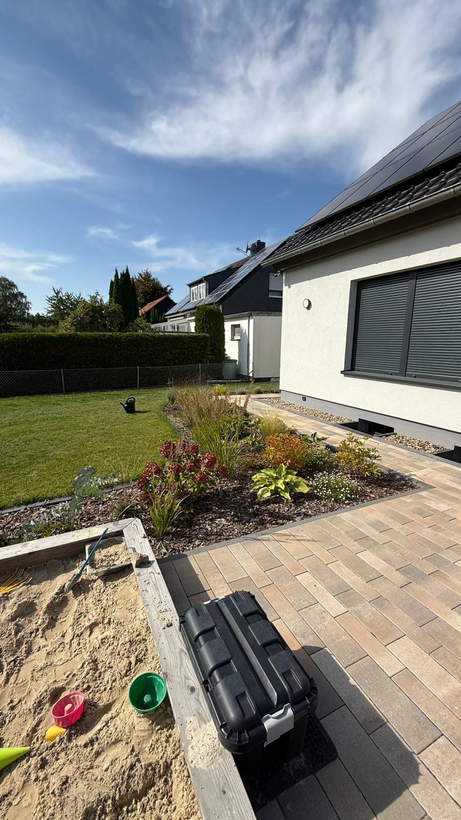 Gartengestaltung mit gepflegtem Rasen, Sandkasten und Blumenrabatte